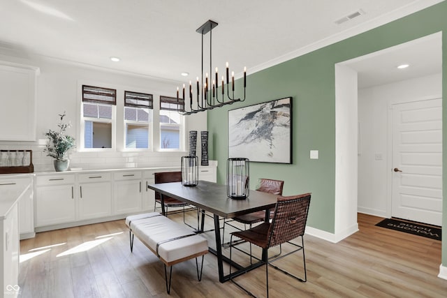 dining space featuring crown molding, a chandelier, and light hardwood / wood-style flooring