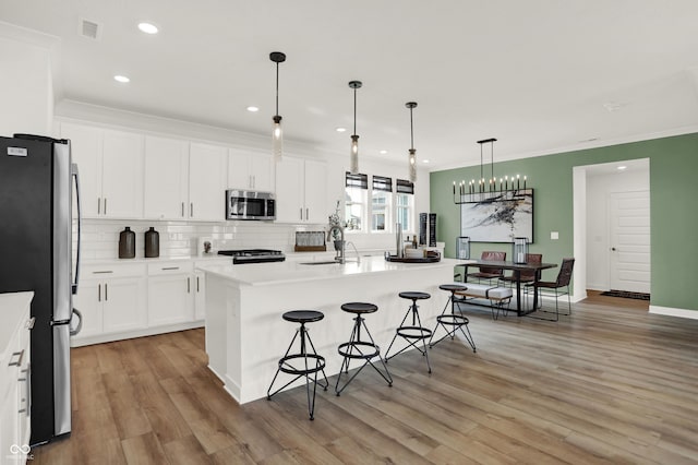 kitchen with appliances with stainless steel finishes, white cabinets, a kitchen breakfast bar, hanging light fixtures, and a kitchen island with sink