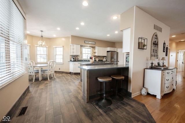 kitchen with dark wood-type flooring, stainless steel fridge, white cabinets, decorative light fixtures, and kitchen peninsula