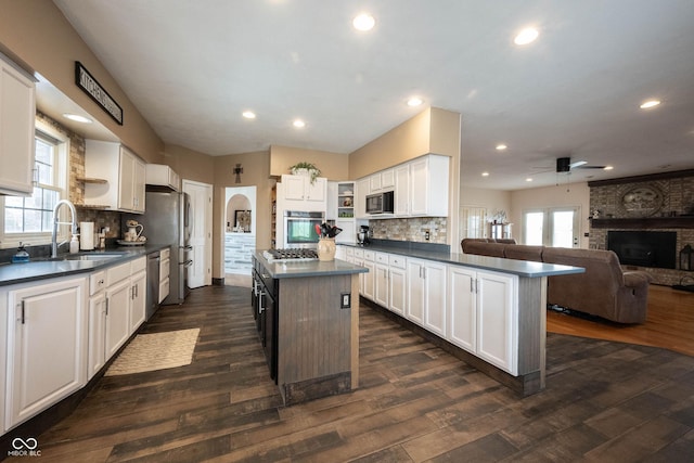 kitchen featuring sink, appliances with stainless steel finishes, white cabinets, a kitchen island, and a brick fireplace