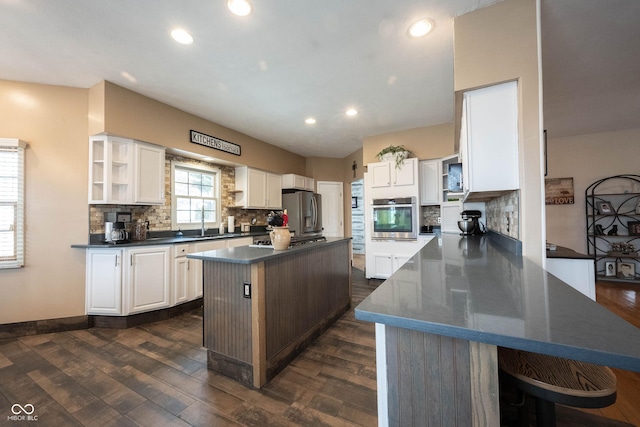 kitchen featuring appliances with stainless steel finishes, tasteful backsplash, white cabinets, a center island, and dark wood-type flooring