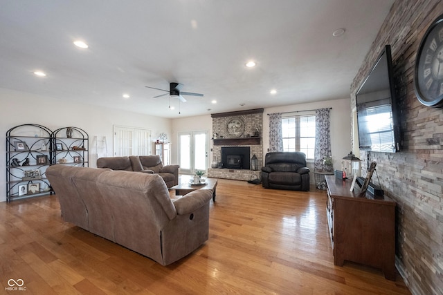 living room featuring ceiling fan, a brick fireplace, and light wood-type flooring