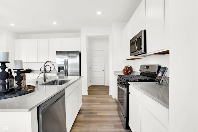 kitchen with appliances with stainless steel finishes, light hardwood / wood-style floors, sink, and white cabinets