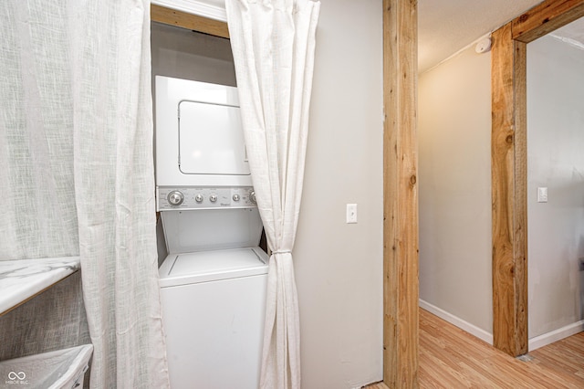 clothes washing area with light hardwood / wood-style flooring and stacked washer and clothes dryer