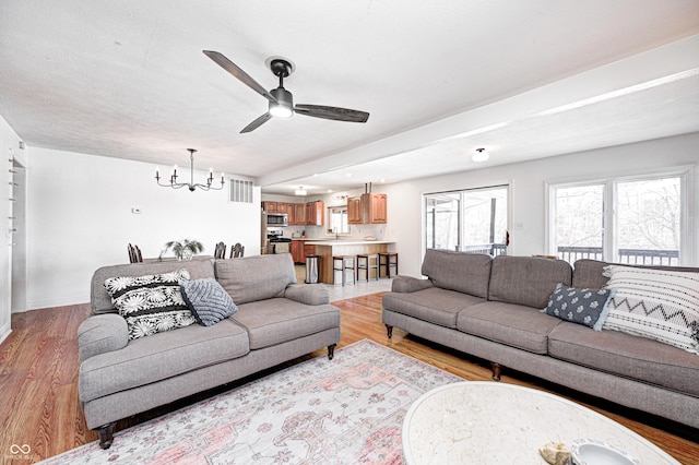 living room featuring ceiling fan with notable chandelier and light wood-type flooring