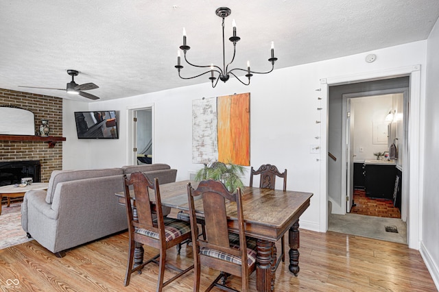 dining area featuring ceiling fan with notable chandelier, a fireplace, a textured ceiling, and light wood-type flooring