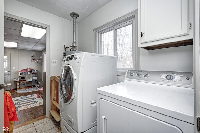 clothes washing area featuring cabinets, washing machine and clothes dryer, and light tile patterned floors