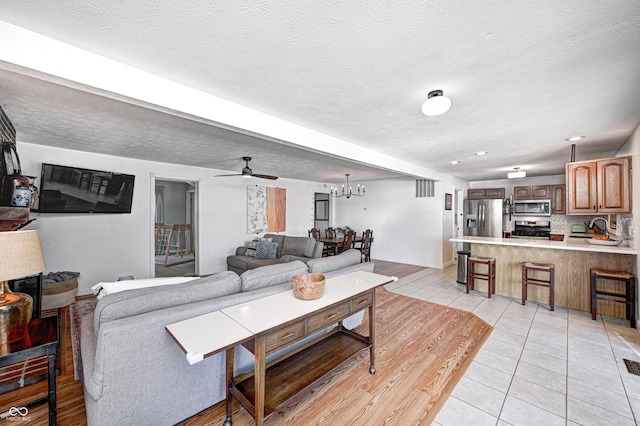 tiled living room with ceiling fan with notable chandelier, sink, and a textured ceiling