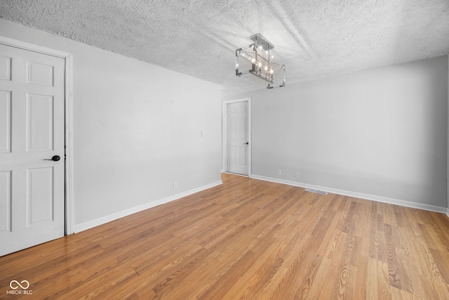 empty room featuring light hardwood / wood-style floors, a textured ceiling, and a notable chandelier