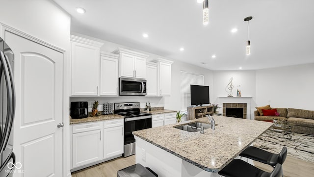 kitchen featuring stainless steel appliances, an island with sink, hanging light fixtures, and white cabinetry