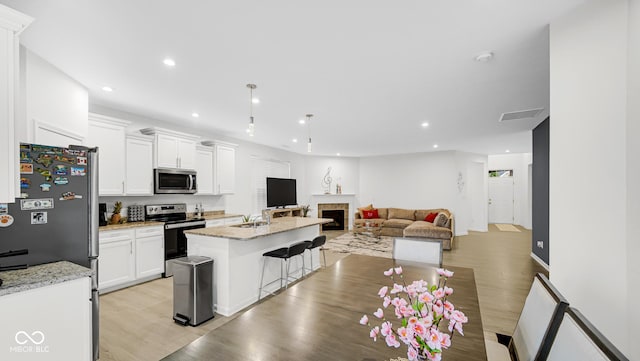 kitchen with white cabinetry, stainless steel appliances, a kitchen island with sink, and light stone counters