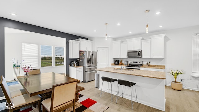 kitchen featuring appliances with stainless steel finishes, white cabinets, hanging light fixtures, a kitchen island with sink, and light stone countertops