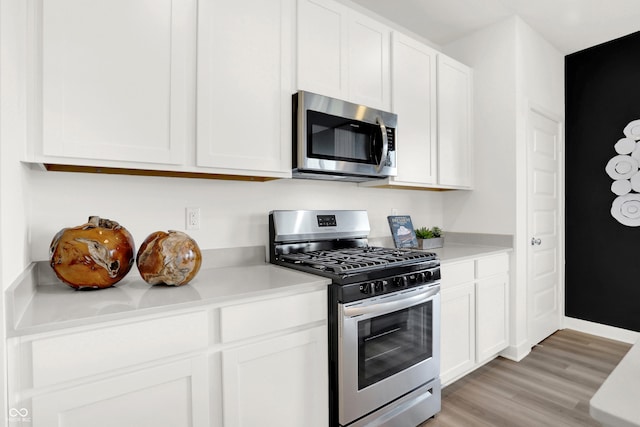 kitchen with appliances with stainless steel finishes, white cabinets, and light hardwood / wood-style floors