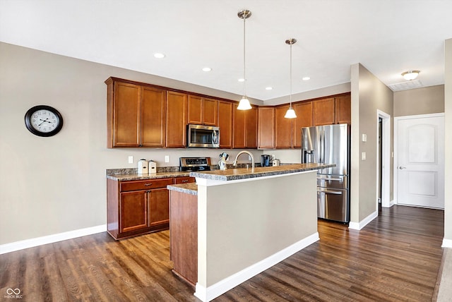 kitchen featuring decorative light fixtures, dark hardwood / wood-style flooring, light stone counters, stainless steel appliances, and a center island with sink