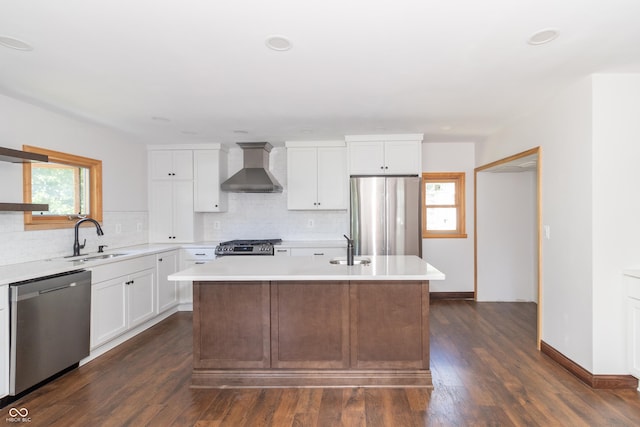 kitchen featuring wall chimney range hood, sink, appliances with stainless steel finishes, white cabinetry, and a kitchen island