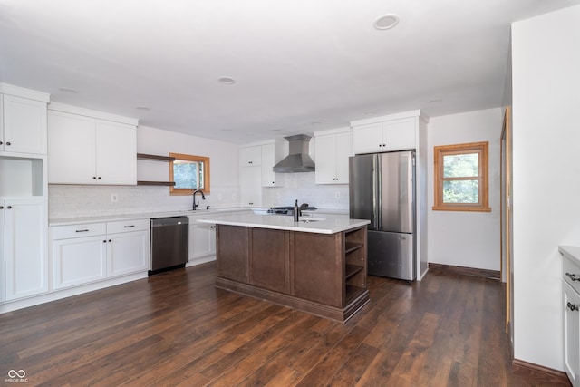 kitchen with wall chimney exhaust hood, white cabinetry, dark hardwood / wood-style floors, an island with sink, and stainless steel appliances