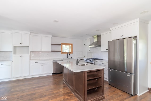 kitchen with sink, a center island with sink, wall chimney range hood, stainless steel appliances, and white cabinets