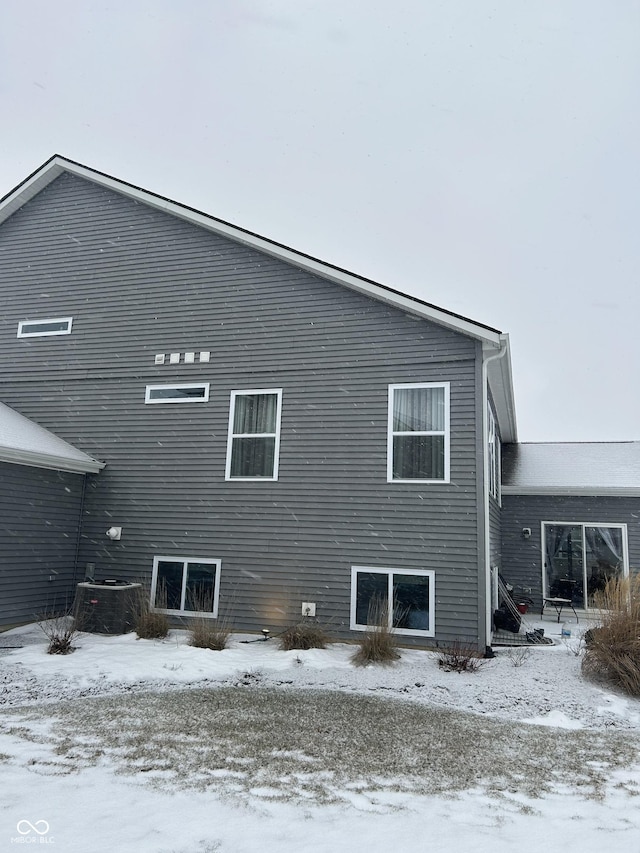 snow covered rear of property featuring central AC