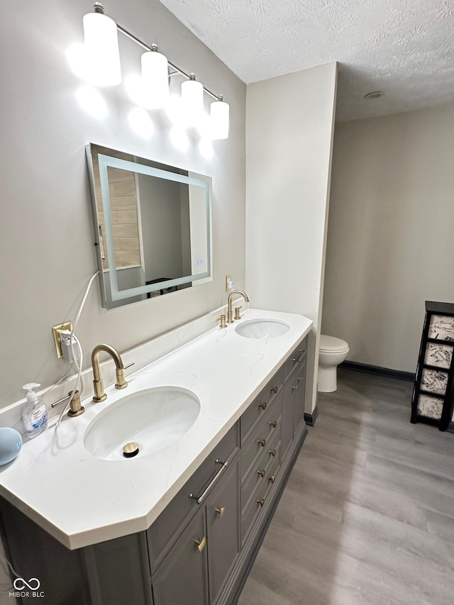 bathroom with vanity, toilet, wood-type flooring, and a textured ceiling