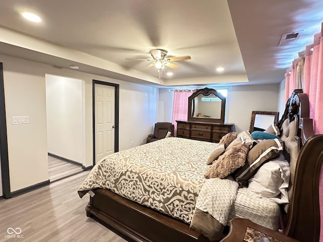 bedroom with light hardwood / wood-style flooring, ceiling fan, and a tray ceiling