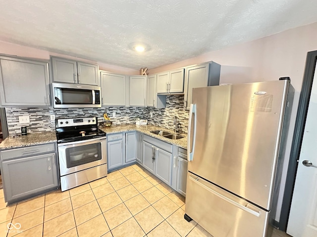 kitchen featuring stainless steel appliances, sink, gray cabinetry, and stone counters