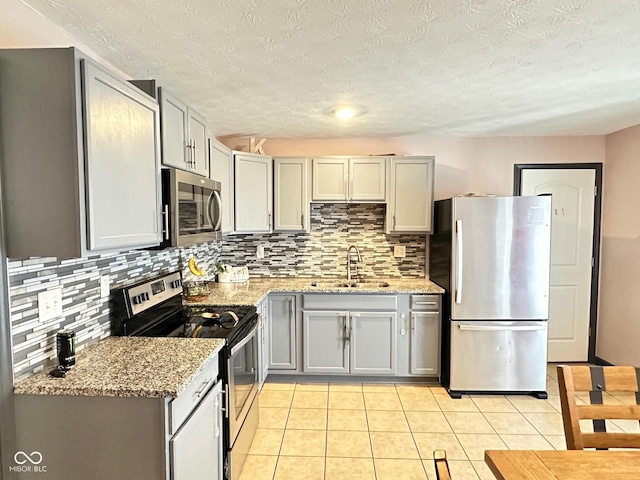 kitchen with sink, appliances with stainless steel finishes, gray cabinetry, light stone counters, and light tile patterned flooring