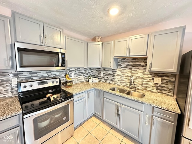 kitchen featuring sink, gray cabinetry, light tile patterned floors, stainless steel appliances, and light stone countertops