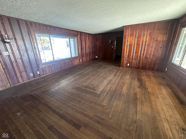 unfurnished room with dark parquet floors, wooden walls, and a textured ceiling