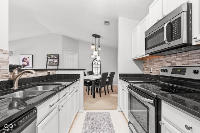 kitchen with sink, appliances with stainless steel finishes, white cabinetry, hanging light fixtures, and dark stone countertops