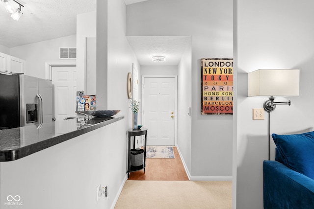 kitchen with stainless steel fridge, kitchen peninsula, a textured ceiling, and white cabinets