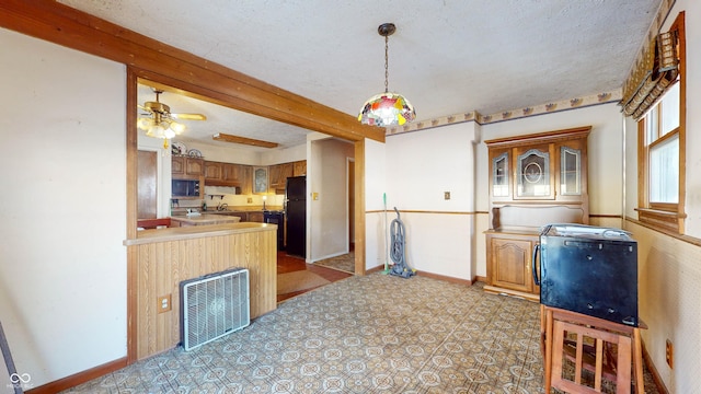 kitchen featuring pendant lighting, beamed ceiling, black appliances, and a textured ceiling