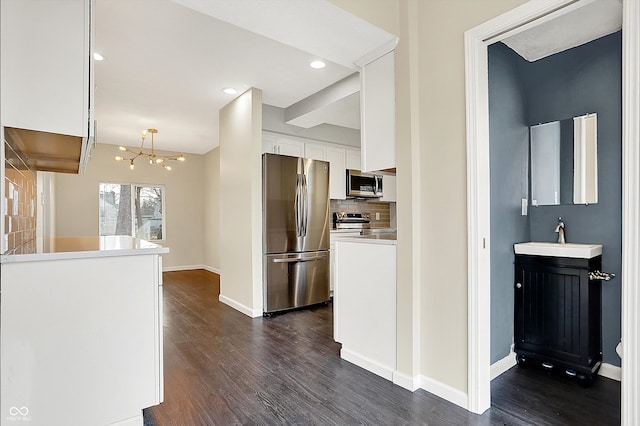 kitchen featuring dark wood finished floors, backsplash, appliances with stainless steel finishes, white cabinetry, and a sink