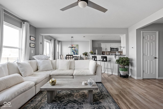 living room with ceiling fan, a textured ceiling, and light wood-type flooring