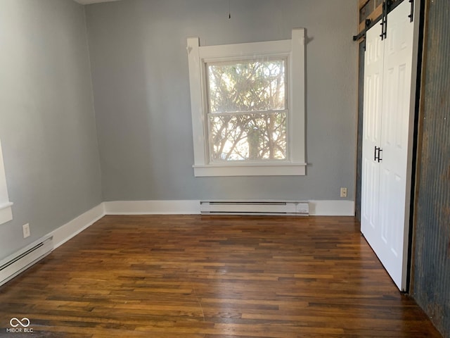 spare room with dark wood-type flooring, a baseboard radiator, and a barn door