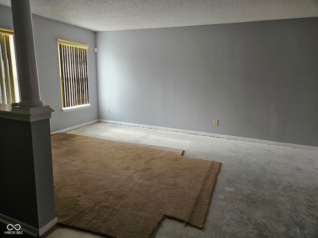 unfurnished room with carpet flooring, decorative columns, and a textured ceiling