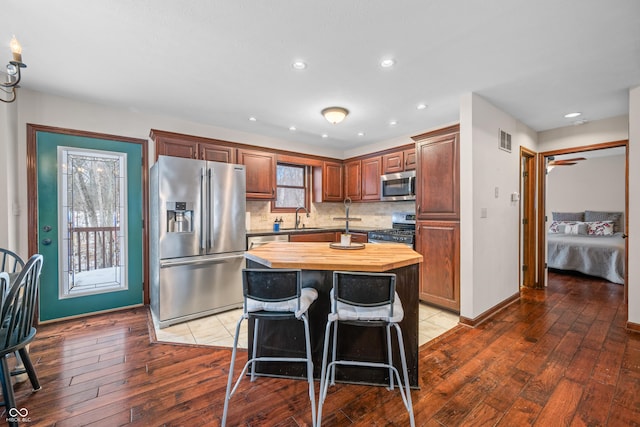 kitchen with hardwood / wood-style flooring, a breakfast bar area, butcher block counters, stainless steel appliances, and a kitchen island