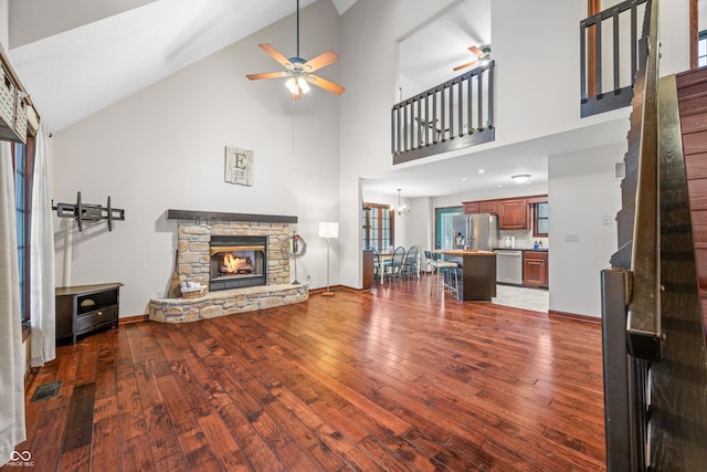 living room with hardwood / wood-style floors, ceiling fan with notable chandelier, a stone fireplace, and high vaulted ceiling