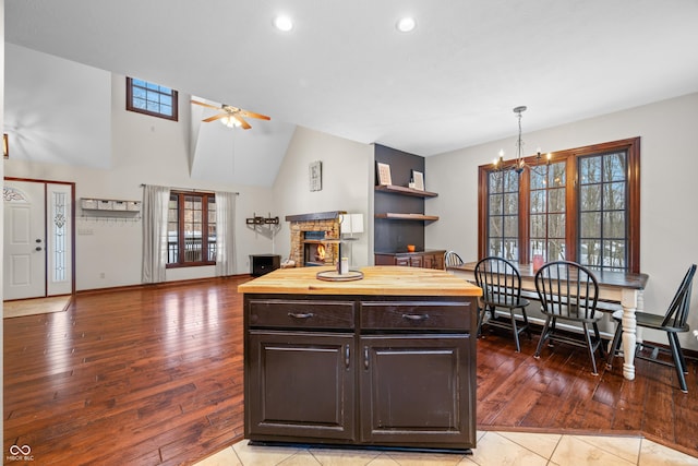 kitchen featuring butcher block counters, dark brown cabinets, a fireplace, a kitchen island, and ceiling fan with notable chandelier