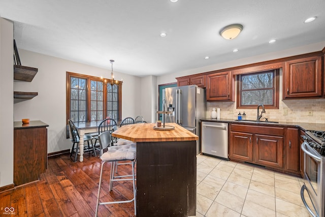 kitchen featuring appliances with stainless steel finishes, butcher block counters, hanging light fixtures, a kitchen bar, and a kitchen island