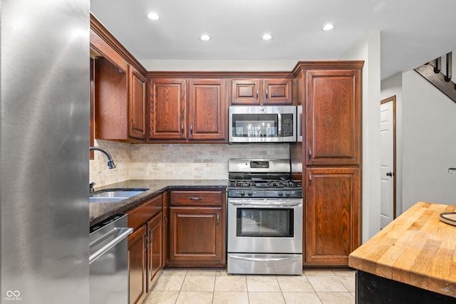 kitchen with sink, appliances with stainless steel finishes, dark stone countertops, backsplash, and light tile patterned flooring