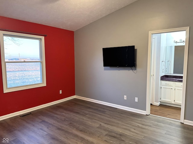 empty room featuring lofted ceiling, dark hardwood / wood-style floors, and a textured ceiling