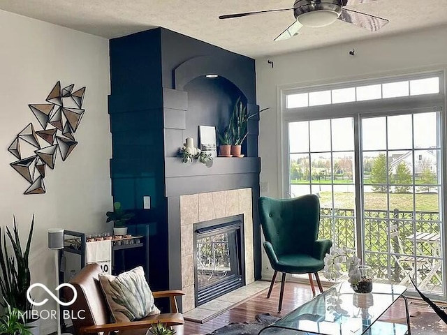 living area featuring ceiling fan, hardwood / wood-style floors, and a tile fireplace