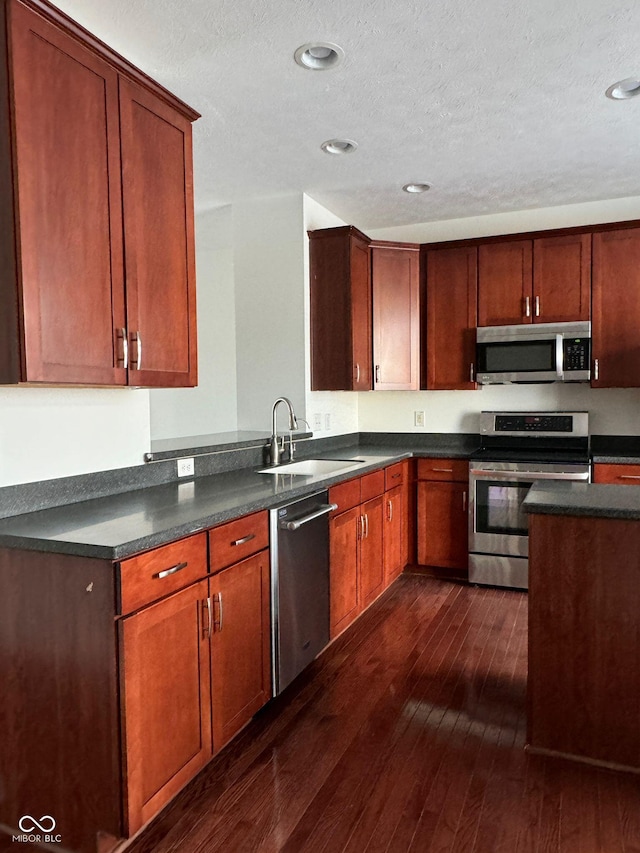 kitchen with sink, dark wood-type flooring, appliances with stainless steel finishes, a textured ceiling, and kitchen peninsula