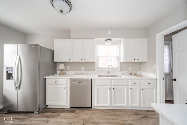 kitchen with white cabinets, appliances with stainless steel finishes, light countertops, light wood-type flooring, and a sink