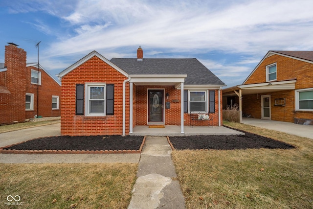 bungalow featuring a shingled roof, a chimney, a front lawn, and brick siding