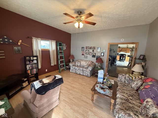 living room with lofted ceiling, ceiling fan, light hardwood / wood-style flooring, and a textured ceiling