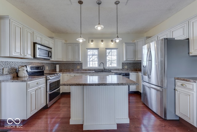 kitchen featuring sink, hanging light fixtures, stainless steel appliances, white cabinets, and a kitchen island