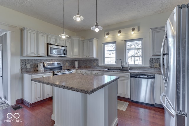 kitchen featuring sink, appliances with stainless steel finishes, hanging light fixtures, dark hardwood / wood-style floors, and a center island