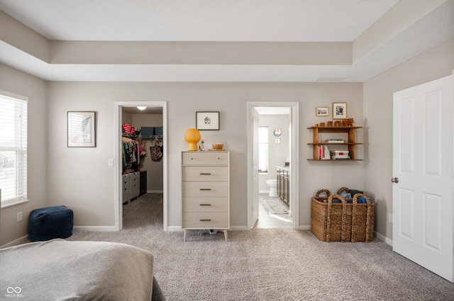 carpeted bedroom featuring a tray ceiling, connected bathroom, a spacious closet, and a closet