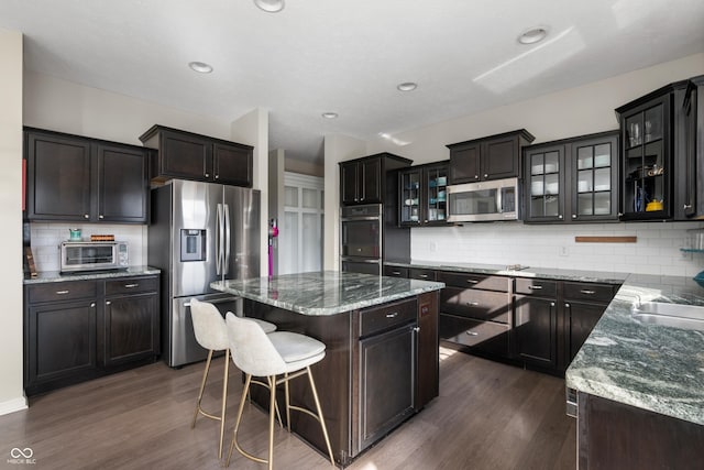 kitchen featuring dark brown cabinets, appliances with stainless steel finishes, dark hardwood / wood-style floors, a kitchen island, and decorative backsplash